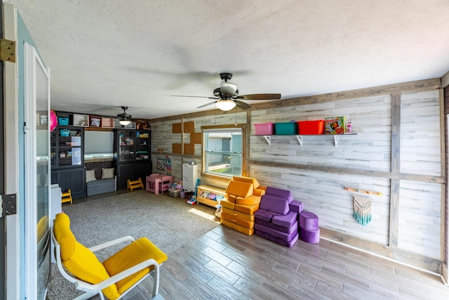 sitting room with a textured ceiling, ceiling fan, and wooden walls