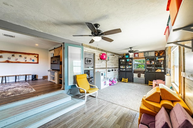 playroom featuring a textured ceiling, ceiling fan, and wood walls