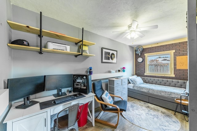 home office with a textured ceiling, light hardwood / wood-style floors, ceiling fan, and brick wall