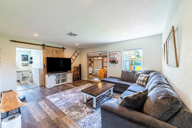 living room with dark hardwood / wood-style flooring, a barn door, a textured ceiling, and ceiling fan