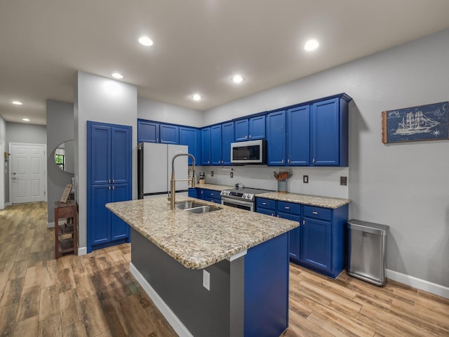 kitchen featuring stainless steel range with electric cooktop, a kitchen island with sink, blue cabinets, sink, and white fridge