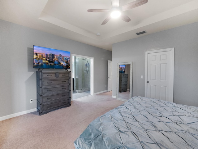 carpeted bedroom with a tray ceiling, ensuite bath, and ceiling fan