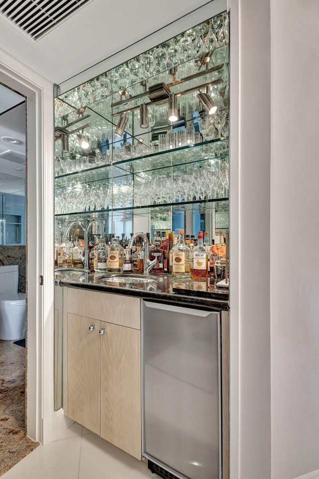 bar featuring dark stone countertops, sink, light tile patterned flooring, and light brown cabinetry