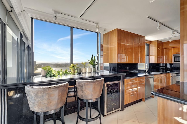 kitchen featuring appliances with stainless steel finishes, track lighting, light tile patterned floors, wine cooler, and a breakfast bar area