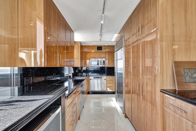 kitchen with sink, rail lighting, dark stone countertops, light tile patterned floors, and appliances with stainless steel finishes