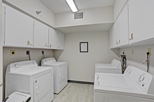 washroom featuring washing machine and dryer, cabinets, a textured ceiling, and light wood-type flooring