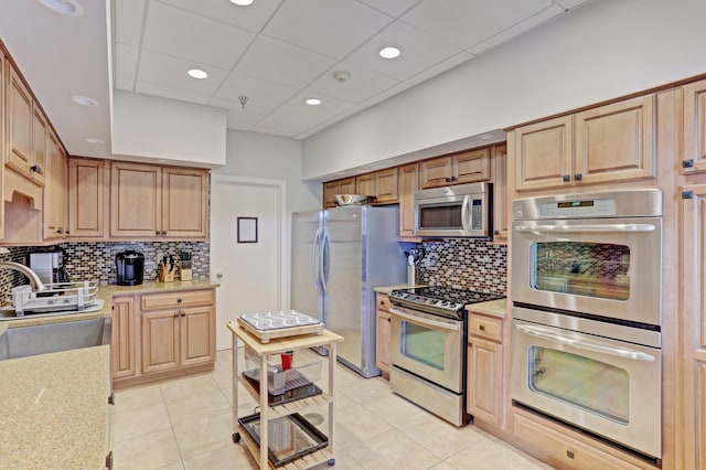 kitchen with a paneled ceiling, tasteful backsplash, stainless steel appliances, sink, and light tile patterned flooring