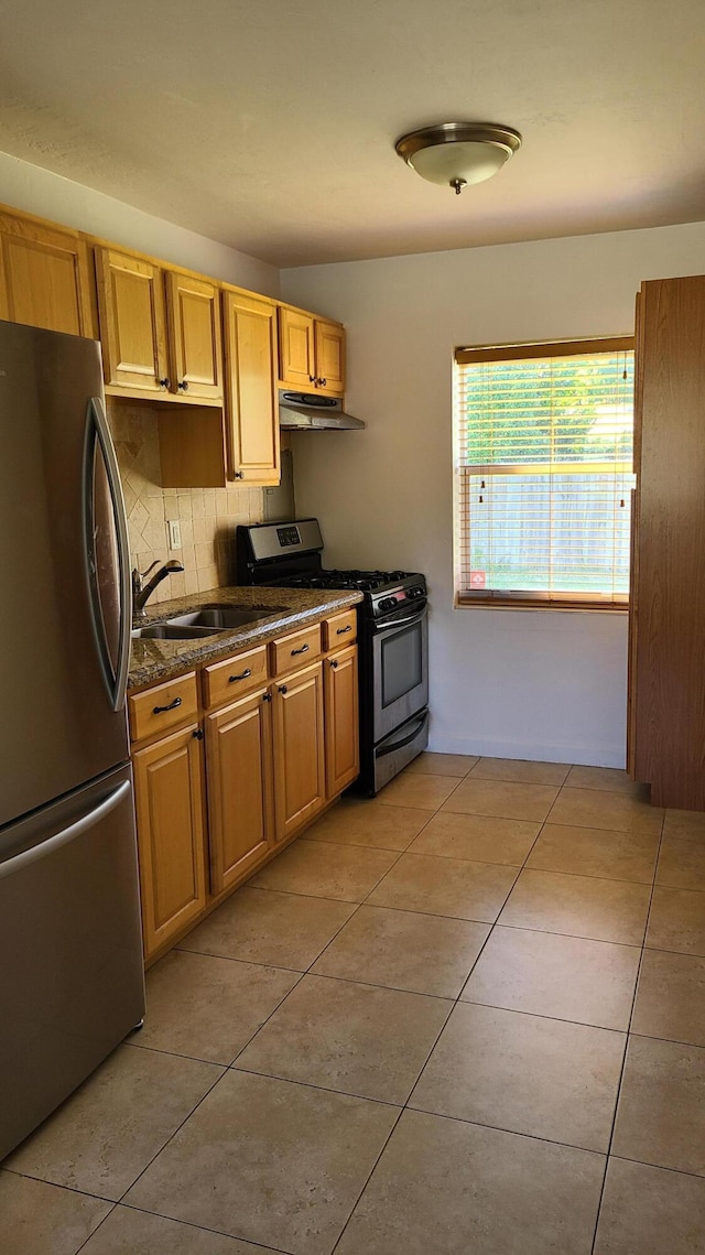 kitchen with stainless steel refrigerator, sink, gas range oven, dark stone counters, and light tile patterned floors