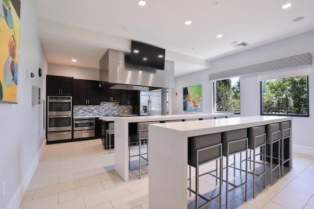 kitchen with appliances with stainless steel finishes, a breakfast bar area, backsplash, a large island, and exhaust hood