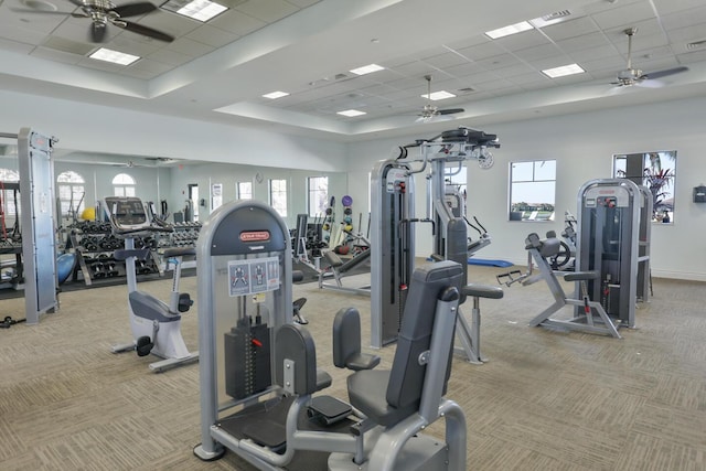 gym with light carpet, a raised ceiling, and a ceiling fan