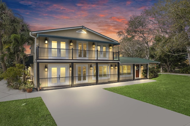 back house at dusk with a lawn, french doors, and a balcony