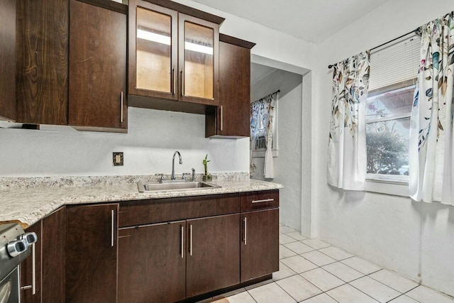 kitchen featuring sink, light stone counters, dark brown cabinets, light tile patterned flooring, and range