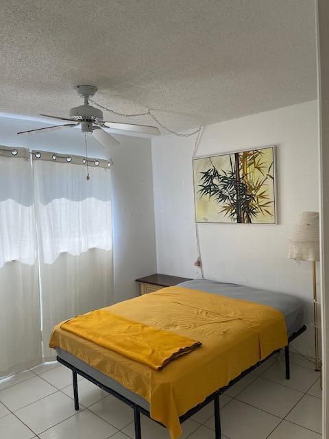 tiled bedroom with ceiling fan and a textured ceiling