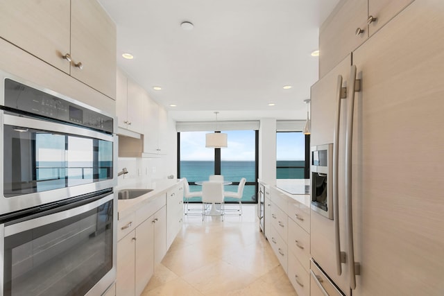 kitchen with sink, a water view, stainless steel double oven, and decorative light fixtures