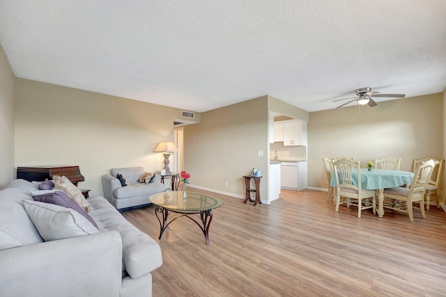 living room with a textured ceiling, light hardwood / wood-style floors, and ceiling fan