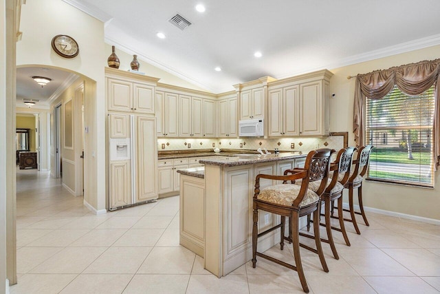 kitchen with tasteful backsplash, light stone countertops, a breakfast bar area, and cream cabinetry