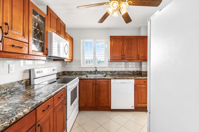 kitchen featuring light tile patterned flooring, sink, dark stone countertops, white appliances, and backsplash