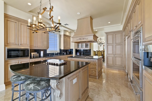 kitchen featuring premium range hood, dark stone counters, stainless steel appliances, a notable chandelier, and a kitchen island