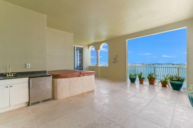 view of patio featuring a water view, a hot tub, exterior kitchen, and sink