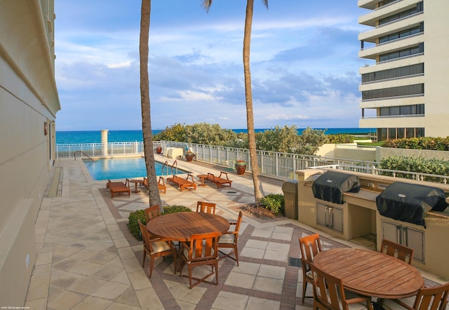 view of patio with area for grilling, a community pool, and a water view