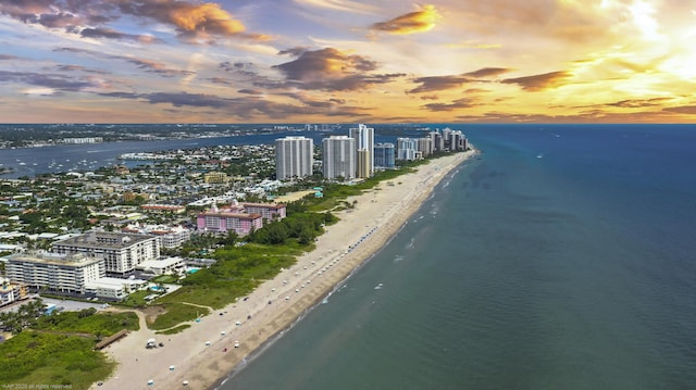 aerial view at dusk featuring a view of the beach and a water view