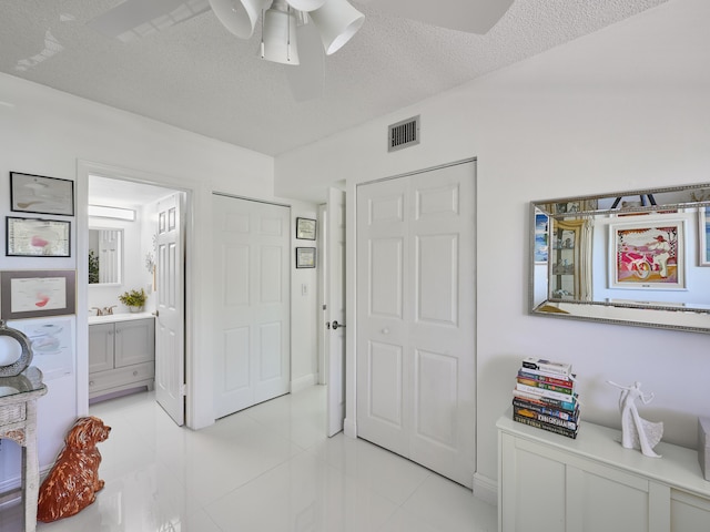 bedroom with light tile patterned floors, a textured ceiling, ensuite bath, and ceiling fan