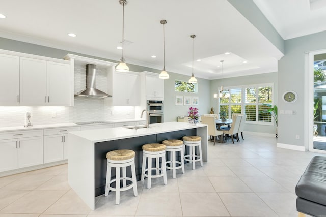 kitchen featuring white cabinetry, pendant lighting, wall chimney exhaust hood, and an island with sink