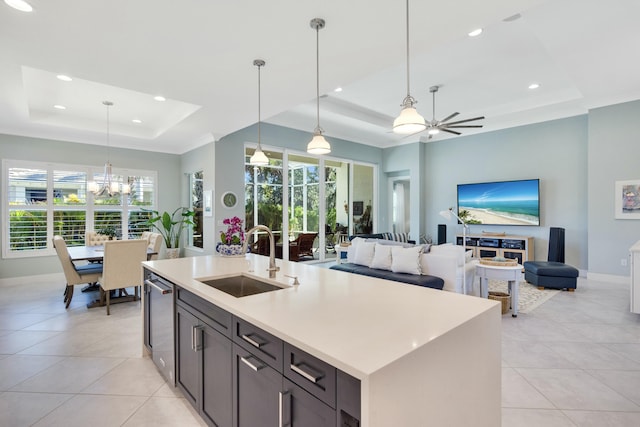 kitchen featuring ceiling fan with notable chandelier, a raised ceiling, sink, pendant lighting, and a center island with sink