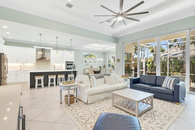 tiled living room featuring ceiling fan, ornamental molding, sink, and a tray ceiling