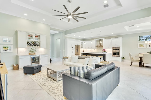 living room with ceiling fan, wet bar, wine cooler, a tray ceiling, and light tile patterned floors