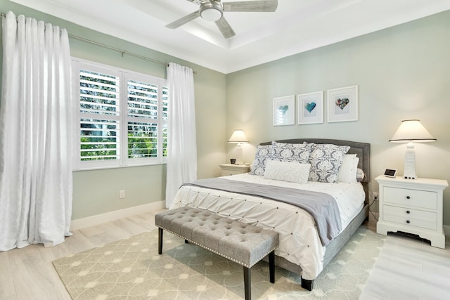 bedroom with ceiling fan, a raised ceiling, and light hardwood / wood-style flooring