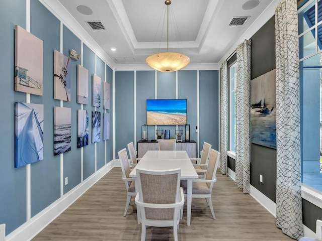 dining room featuring light wood-type flooring, a tray ceiling, and ornamental molding