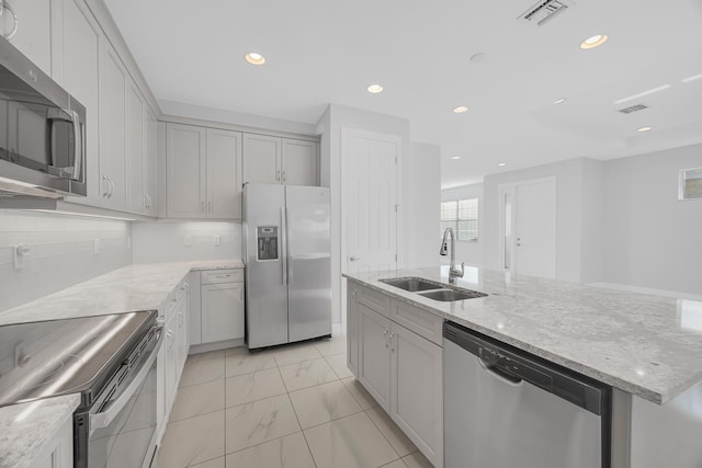 kitchen featuring decorative backsplash, light stone counters, stainless steel appliances, sink, and an island with sink