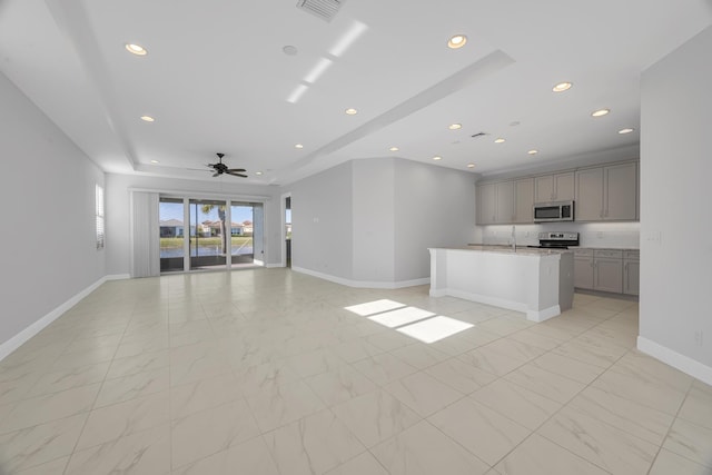 unfurnished living room featuring ceiling fan, sink, and a tray ceiling