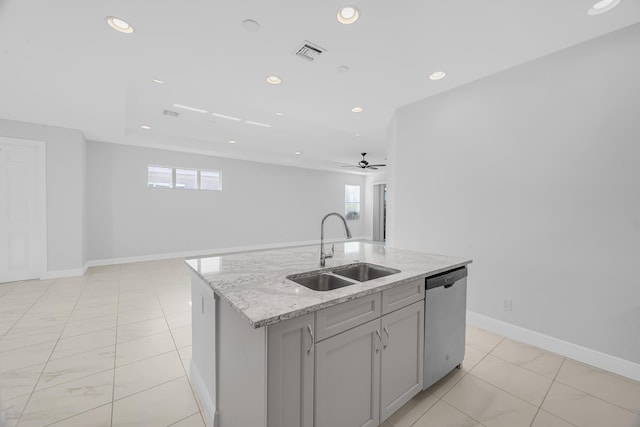 kitchen with ceiling fan, dishwasher, light stone countertops, sink, and an island with sink