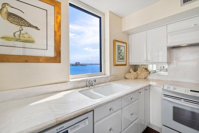 kitchen featuring sink, a textured ceiling, a water view, white cabinets, and range