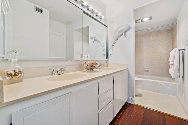 full bathroom featuring a textured ceiling, vanity, toilet, and tiled shower / bath