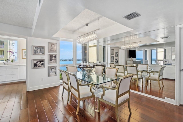 dining space with a tray ceiling, a textured ceiling, a chandelier, and dark hardwood / wood-style floors