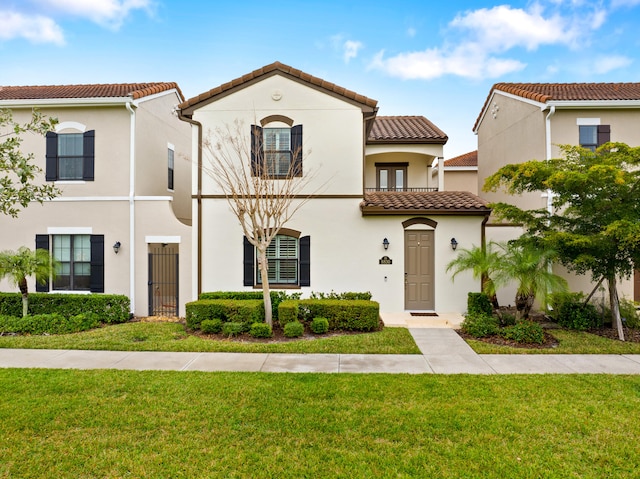 mediterranean / spanish house with stucco siding, a tile roof, and a front lawn