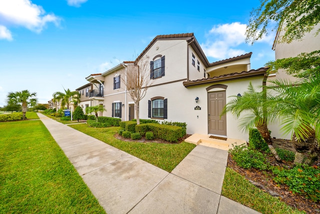 mediterranean / spanish-style home with a front lawn, a tile roof, and stucco siding