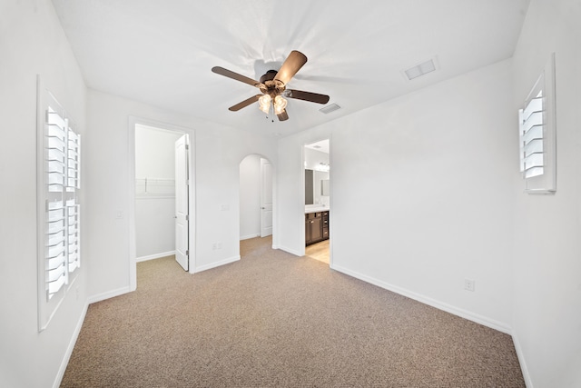 unfurnished bedroom with a closet, a walk in closet, light colored carpet, and ceiling fan