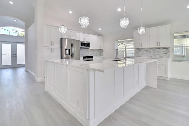 kitchen with white cabinets, a spacious island, hanging light fixtures, decorative backsplash, and appliances with stainless steel finishes