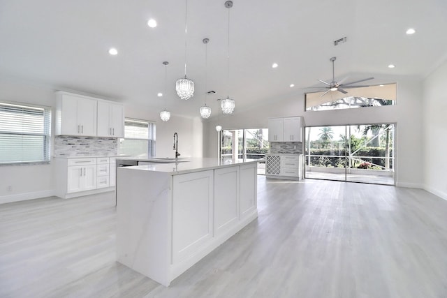 kitchen featuring a kitchen island with sink, white cabinets, sink, tasteful backsplash, and decorative light fixtures