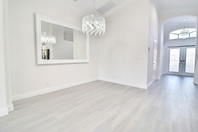 interior space with french doors, light wood-type flooring, crown molding, a notable chandelier, and a high ceiling