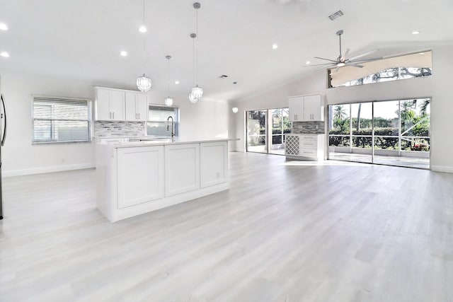 kitchen featuring ceiling fan, hanging light fixtures, an island with sink, decorative backsplash, and white cabinets