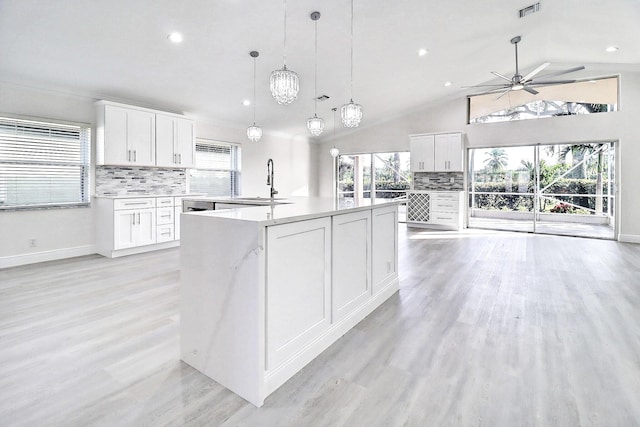 kitchen with white cabinets, lofted ceiling, a kitchen island with sink, and hanging light fixtures