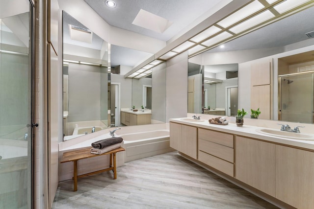 bathroom featuring plus walk in shower, wood-type flooring, vanity, and a skylight