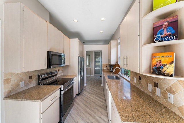 kitchen with backsplash, sink, light wood-type flooring, light stone countertops, and appliances with stainless steel finishes