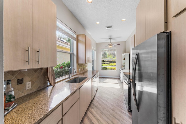 kitchen featuring light brown cabinetry, tasteful backsplash, stainless steel appliances, sink, and stone countertops