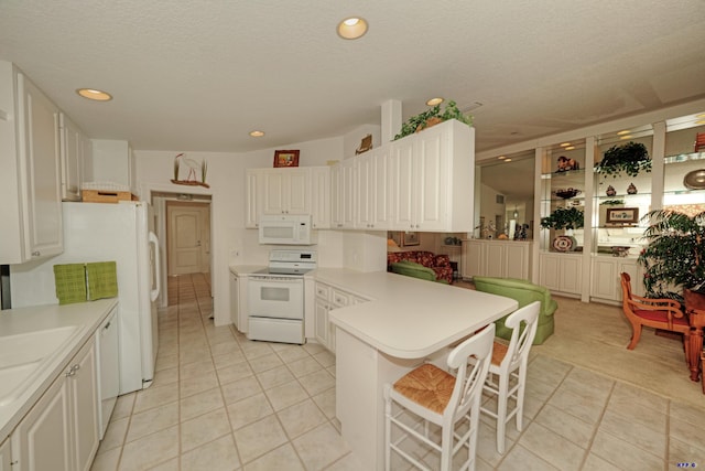 kitchen with white cabinets, white appliances, light tile patterned flooring, and a breakfast bar